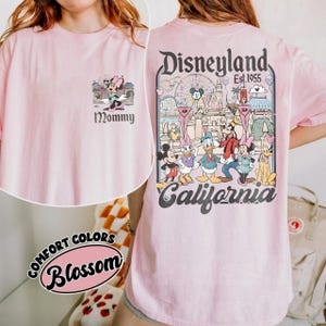 May include: A light pink t-shirt featuring a Minnie Mouse graphic with the word "Mommy" on the front. The back of the shirt displays a Disneyland graphic with various Disney characters and the text "Disneyland Est. 1955 California".