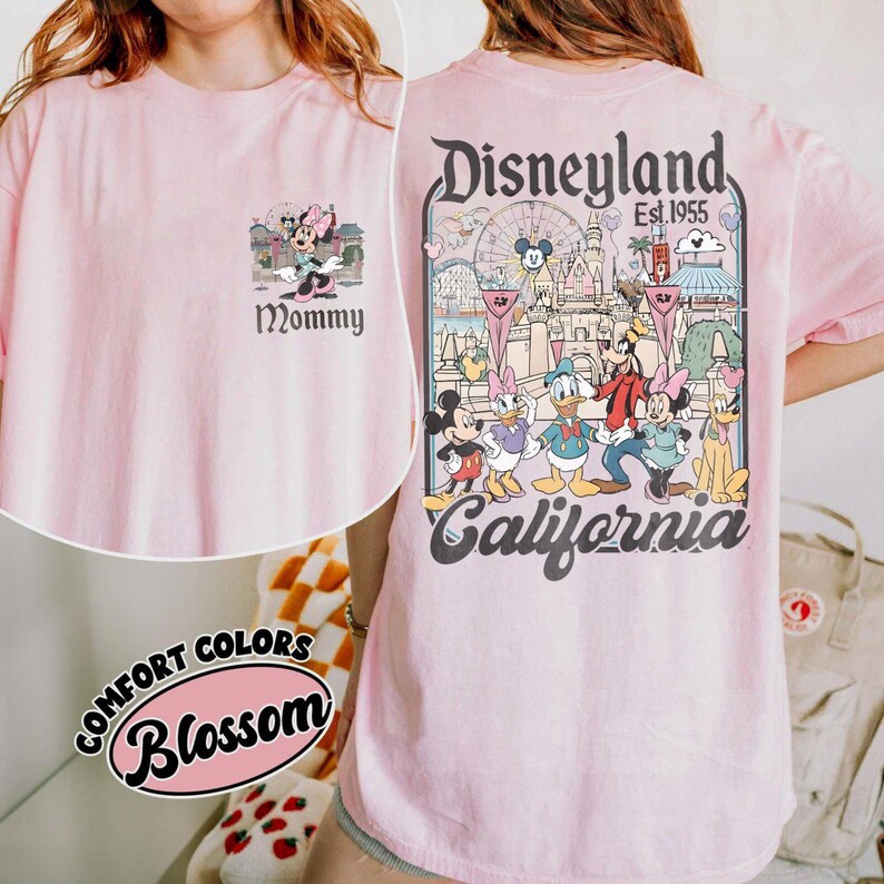 May include: A light pink t-shirt featuring a Minnie Mouse graphic with the word "Mommy" on the front. The back of the shirt displays a Disneyland graphic with various Disney characters and the text "Disneyland Est. 1955 California".