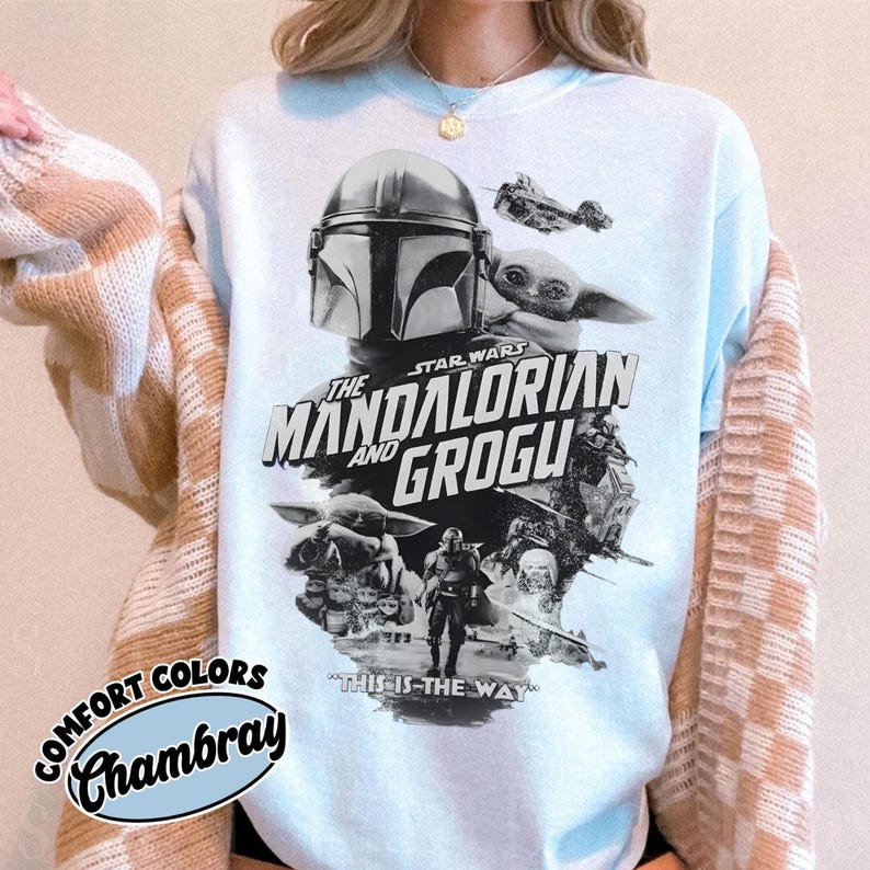 Op de afbeelding: Lichtblauw sweatshirt met een afbeelding uit de Star Wars-serie, "The Mandalorian and Grogu". Het ontwerp bevat de helm van de Mandalorian, Grogu en de zin "This is the Way". Het sweatshirt heeft een "Comfort Colors Chambray" label.