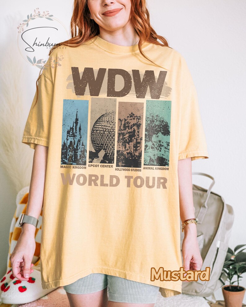May include: A yellow t-shirt with a vintage-style graphic of the Walt Disney World theme parks. The graphic includes the text "WDW World Tour" and images of Magic Kingdom, Epcot Center, Hollywood Studios, and Animal Kingdom.