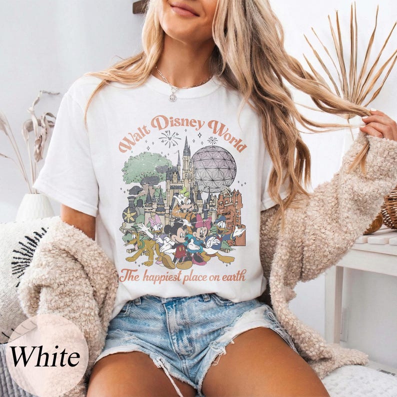 May include: White t-shirt featuring a vintage-style graphic of Walt Disney World with Mickey Mouse, Donald Duck, and other characters. The text "Walt Disney World" and "The happiest place on earth" are printed on the front.
