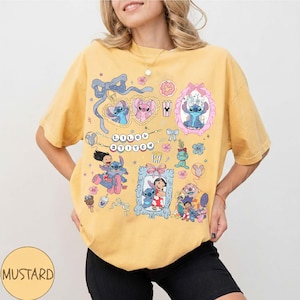 May include: Mustard yellow t-shirt featuring various cartoon images of Stitch and the words "Lilo & Stitch". The shirt has a crew neck and short sleeves. The design includes hearts, bows, and floral accents.