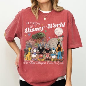 May include: Red t-shirt with a Disney World graphic. The design includes the text "Florida Disney World Est. 1971" with Disney characters and park landmarks. The phrase "The Most Magical Place On Earth" is also included.