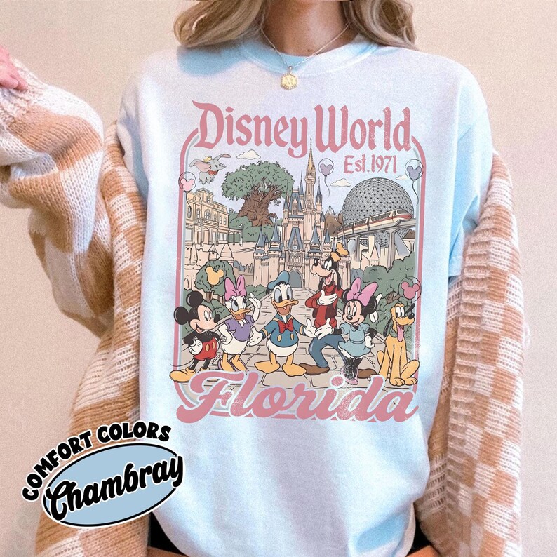 May include: Light blue sweatshirt featuring a Disney World Florida graphic with Mickey Mouse, Minnie Mouse, Donald Duck, Daisy Duck, Goofy, and Pluto. The graphic includes the text "Disney World Est. 1971" and "Florida".