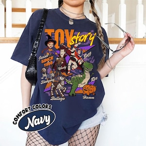 May include: Navy blue t-shirt featuring a graphic of Toy Story characters, including Woody, Buzz Lightyear, and Rex. The shirt has the text "Toy Story" and "Since 1995". The shirt also has the text "Comfort Colors Navy".