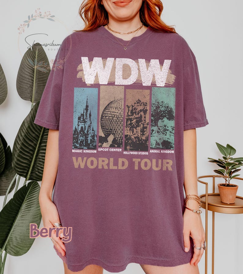 May include: A purple t-shirt with a graphic of the four theme parks at Walt Disney World. The text "WDW World Tour" is printed below the graphic. The parks are Magic Kingdom, Epcot Center, Hollywood Studios, and Animal Kingdom.