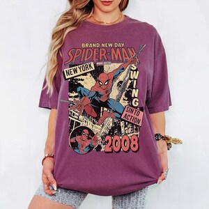May include: A maroon t-shirt with a Spider-Man graphic. The design includes the words "BRAND NEW DAY," "SPIDER-MAN," "NEW YORK," and "SWING INTO ACTION," along with the year "2008." The superhero is shown in a dynamic pose.
