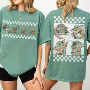 May include: A sage green t-shirt featuring a series of Grogu illustrations with a white and black checkered pattern. The front of the shirt displays Grogu in various poses, while the back showcases four Grogu images.