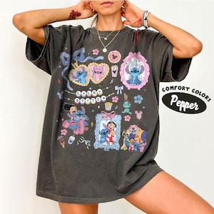 May include: Dark gray t-shirt featuring a colorful graphic of Stitch from Lilo & Stitch. The design includes Stitch in various poses within frames, hearts, and floral elements. The text "Lilo & Stitch" is also present. The shirt has the text "Comfort Colors Pepper".