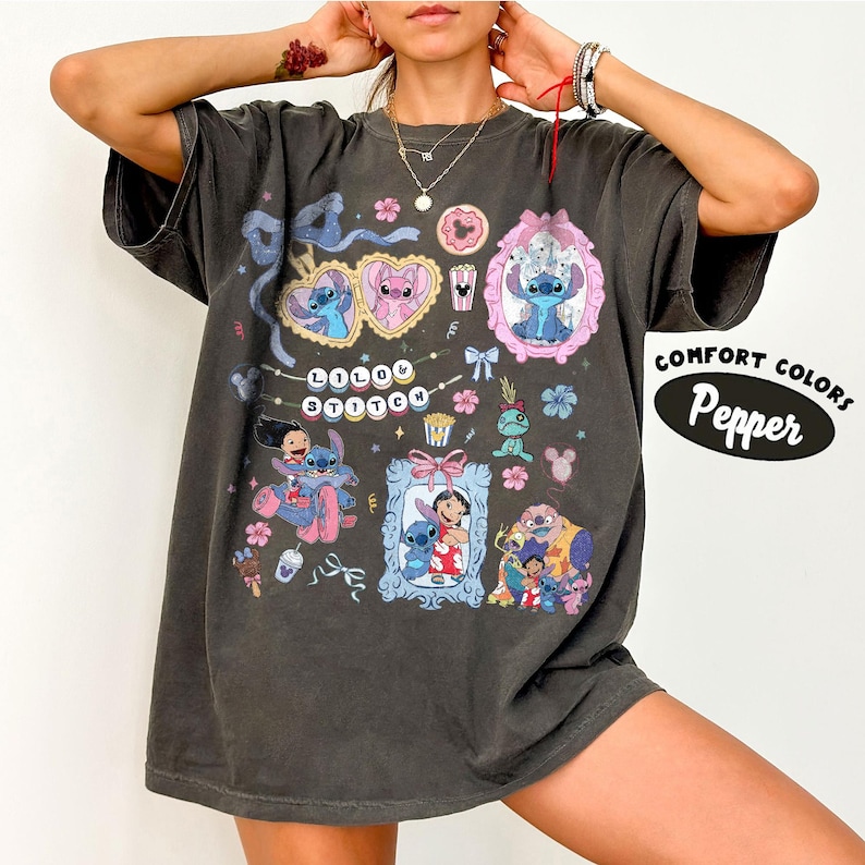 May include: Dark gray t-shirt featuring a colorful graphic of Stitch from Lilo & Stitch. The design includes Stitch in various poses within frames, hearts, and floral elements. The text "Lilo & Stitch" is also present. The shirt has the text "Comfort Colors Pepper".