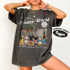May include: Dark grey t-shirt with a Disney World graphic. The design includes the text "Florida Disney World Est. 1971" and cartoon characters such as Mickey and Minnie Mouse. The shirt also has the text "The Most Magical Place On Earth."