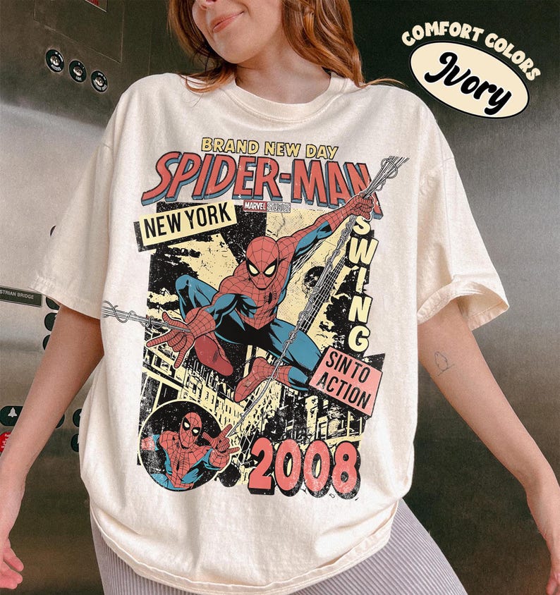 May include: Ivory t-shirt with a Spider-Man graphic. The design includes the words "BRAND NEW DAY," "SPIDER-MAN," "NEW YORK," and "2008." The graphic depicts Spider-Man in action, with the words "SWING" and "SIN TO ACTION."