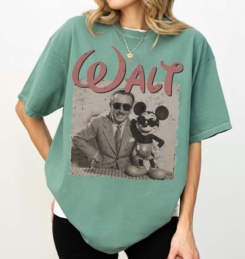 May include: Sage green t-shirt featuring a vintage-style graphic of Walt Disney with Mickey Mouse. The graphic includes the word "Walt" in a pink, cursive font. The shirt is a relaxed fit.