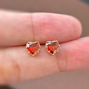 May include: A pair of gold heart-shaped earrings with red gemstones.