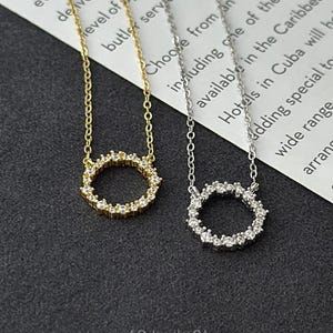 Peut inclure: Deux colliers délicats avec un pendentif rond orné de petites pierres scintillantes. Le collier de gauche a une chaîne dorée et un pendentif rond doré, tandis que le collier de droite a une chaîne argentée et un pendentif rond argenté.