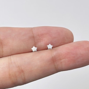 May include: A pair of small, polished silver-toned star-shaped stud earrings. Each earring features a five-pointed star design with a smooth, reflective metallic surface. The earrings are presented as simple, understated jewelry pieces for everyday wear.