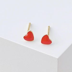 Op de afbeelding: Een paar gouden hartvormige oorbel studs met rood email.