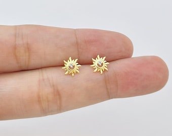Peut inclure: Une paire de boucles d'oreilles clous dorées en forme de soleil. Chaque boucle d'oreille présente une pierre précieuse transparente centrale et des rayons rayonnants. Les boucles d'oreilles sont petites et délicates, adaptées au quotidien.