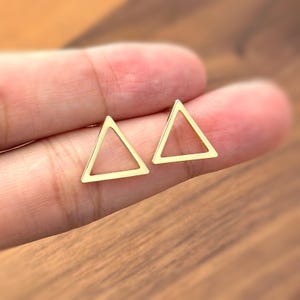 May include: A pair of gold triangle stud earrings. The earrings are simple and minimalist, and would make a great gift for a friend or loved one.