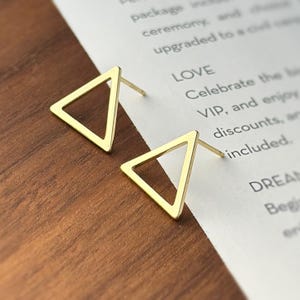 May include: A pair of gold triangle stud earrings. The earrings are simple and minimalist, with a hollow triangle design.