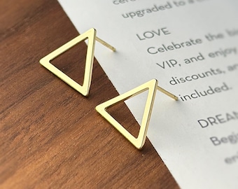 Puede incluir: Un par de pendientes de triángulo de oro. Los pendientes son simples y minimalistas, con un diseño de triángulo hueco.
