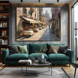 May include: A green velvet sofa with two throw pillows, a coffee table with a vase of dried flowers, and a painting of a street scene in Venice, Italy. The painting features a cafe with tables and chairs, and people walking down the street.