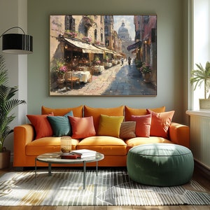 May include: A painting of a street scene in a European city. The street is lined with buildings and there are people walking by. There are tables and chairs set up outside of a cafe. The painting is done in a realistic style and has a warm, inviting feel.