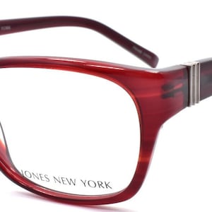 May include: Dark red, translucent rectangular eyeglasses with a subtle horizontal striped pattern. The frames feature silver-toned metal accents on the temples near the hinges. The text JONES NEW YORK is printed on the right lens.
