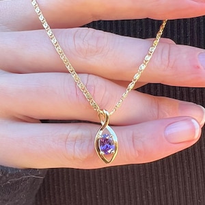 May include: A gold chain necklace with a pendant featuring a purple gemstone set in a gold swirl design.