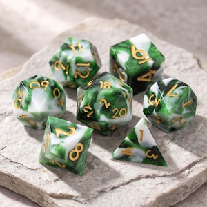 May include: A set of seven polyhedral dice featuring a marbled pattern of deep forest green and opaque white resin. Each die has engraved numbers filled with metallic gold ink, including a twenty-sided die, a twelve-sided die, and others.