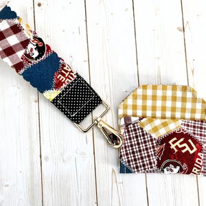 May include: A patchwork lanyard and matching cardholder featuring various fabric patterns, including gingham and polka dots. The lanyard has a metal clasp and a repeating pattern with the text "STATE" and a logo. The cardholder has a similar design.