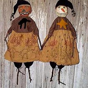 May include: Two primitive rag dolls, one dressed as a pumpkin and the other as a snowman, stand side-by-side. Both dolls have embroidered details and are holding hands. The pumpkin doll has a black hat and a brown dress with a black bird design. The snowman doll has a black hat and a plaid dress with a yellow star. Both dolls have brown twig legs.