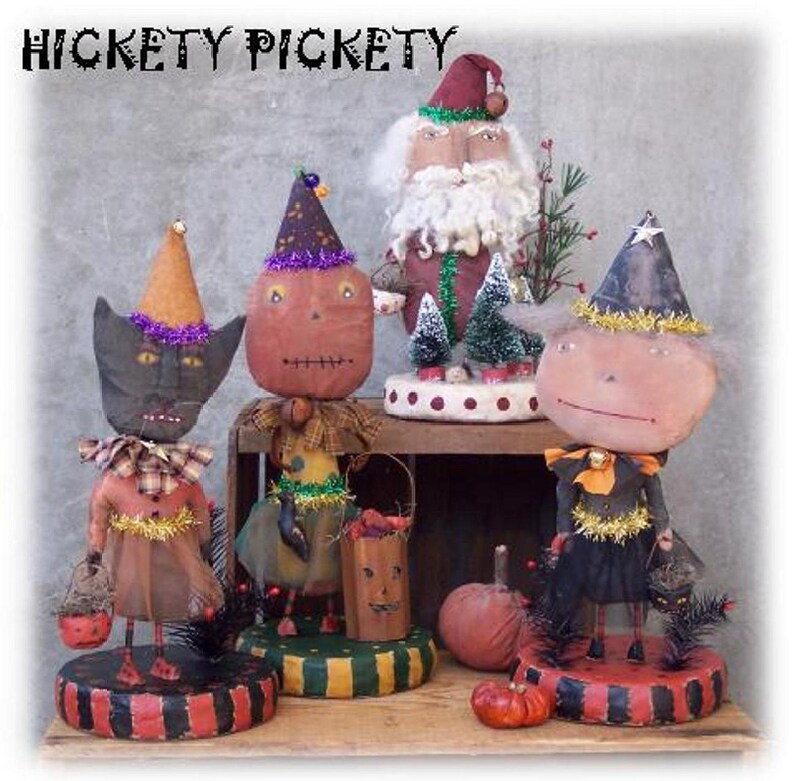 Może przedstawiać: Pięć ręcznie robionych dekoracji halloweenowych, w tym czarny kot, lalka z dynią na twarzy, czarownica i Święty Mikołaj. Dekoracje są wszystkie ubrane w świąteczne stroje i mają kapryśny, vintage'owy styl.