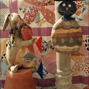 May include: A handmade Easter bunny and egg decoration. The bunny is made of fabric and has a carrot in its hand. The egg is painted with a colorful design and has a black and white face. Both are displayed against a colorful patchwork quilt.