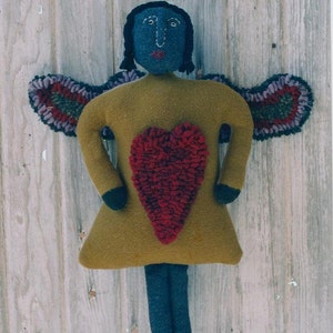 Könnte beinhalten: Ein Filzengel mit blauem Gesicht, braunen Haaren und einem roten Herzen auf der Brust. Der Engel hat lila und grüne Flügel.