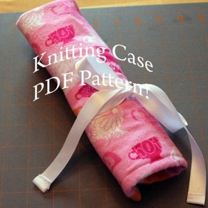 May include: A rolled-up pink knitting case with a white ribbon tied around it. The case is patterned with flowers and teacups. The text "Knitting Case PDF Pattern!" is printed on the case.