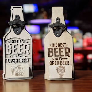 May include: Two wooden bottle openers shaped like beer bottles. The bottle openers have a black metal bottle opener attached to the neck of the bottle. The text on the bottle openers reads "The best beer is an open beer". One bottle opener has a small card with a beer glass and the text "Save water drink beer". The other bottle opener has a small card with a werewolf graphic.