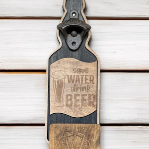 Op de afbeelding: Houten flessenopener in de vorm van een bierfles met een metalen flessenopener aan de bovenkant. De flessenopener heeft de tekst "Save Water Drink Beer" en een afbeelding van een bierglas. De onderkant van de flessenopener heeft een kleine houten onderzetter met een afbeelding van twee bierglazen.