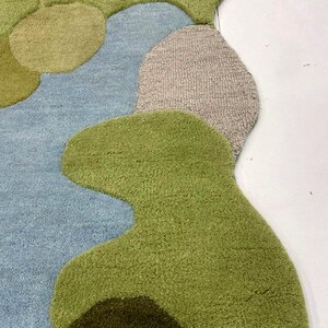 May include: A colorful, abstract rug with a unique, organic shape. The rug features a combination of green, blue, and tan hues, creating a visually appealing design. The rug's texture appears soft and inviting, perfect for adding a touch of style to any room.