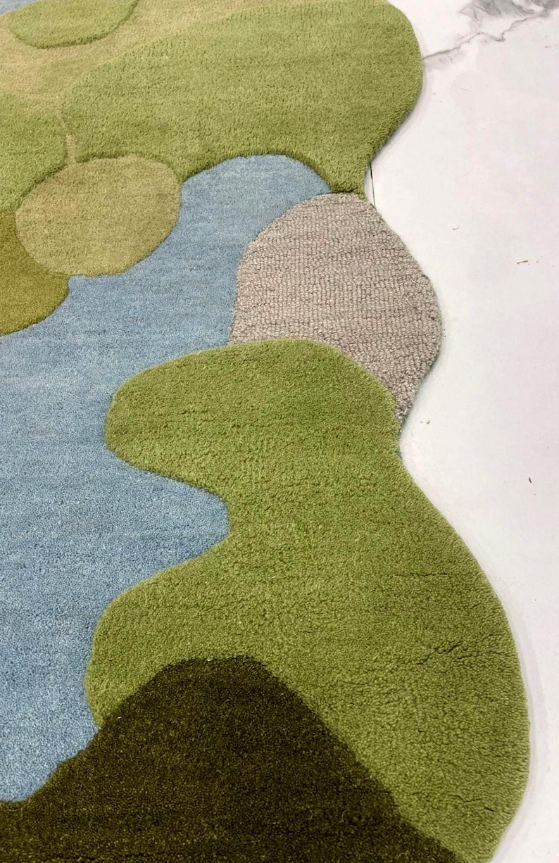 May include: A colorful, abstract rug with a unique, organic shape. The rug features a combination of green, blue, and tan hues, creating a visually appealing design. The rug's texture appears soft and inviting, perfect for adding a touch of style to any room.