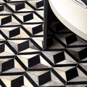 May include: Geometric patterned rug with a 3D cube design in black, white, and tan. The rug is made of a textured material and is partially visible under a white round table.