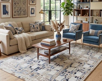 May include: A living room scene featuring a beige sofa with patterned pillows and a cream-colored throw. Two blue armchairs flank a wooden coffee table. A large rug with a geometric pattern in blue, beige, and brown tones covers the floor. Artwork hangs on the wall.