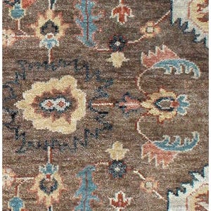 Macro view of hand-knotted wool fibers showing the intricate brown and blue floral Oushak pattern details.