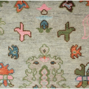 May include: Close-up of a gray rug with a repeating pattern of colorful floral and geometric shapes. The design includes pink, green, orange, and blue elements, creating a textured, decorative surface.