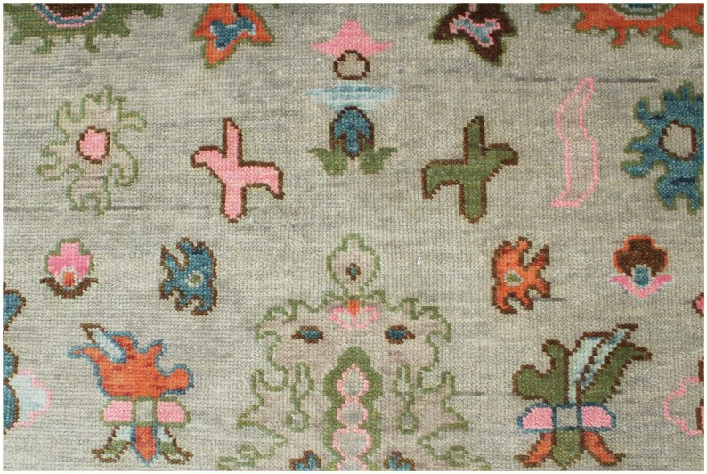 May include: Close-up of a gray rug with a repeating pattern of colorful floral and geometric shapes. The design includes pink, green, orange, and blue elements, creating a textured, decorative surface.