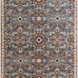 May include: A rectangular area rug with an intricate, symmetrical pattern. The rug features a light blue background with a repeating design in shades of red, brown, and cream. The border is a cream color with a repeating pattern.