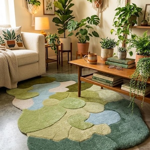 May include: A living room scene featuring a large, abstract-shaped rug in shades of green and blue. The room is decorated with various potted plants, a cream-colored sofa, and wooden furniture. Decorative macrame plant hangers and framed botanical prints adorn the walls.