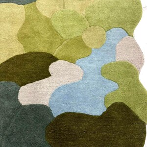 May include: A colorful area rug with an abstract design. The rug features various organic shapes in shades of green, blue, and beige. The rug's texture appears soft and plush, with a high pile. The design is reminiscent of a landscape or a map.