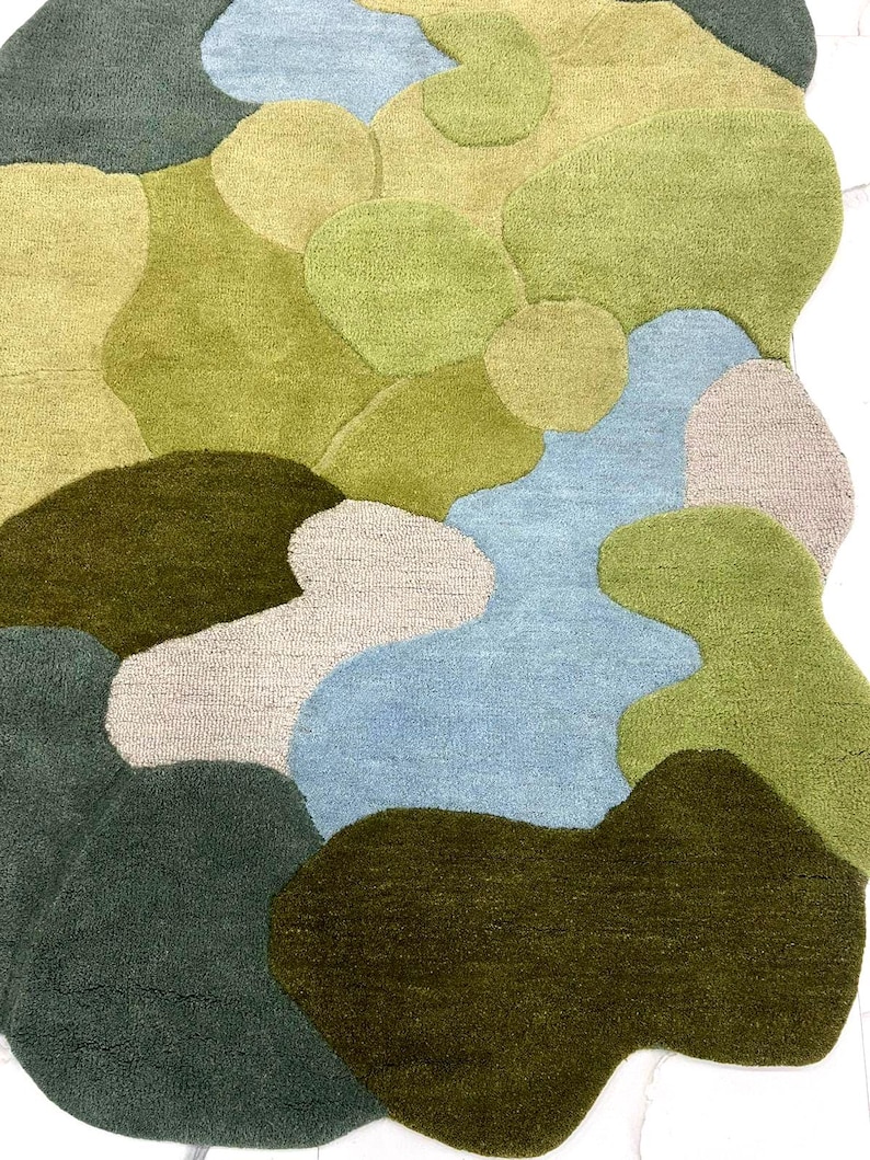 May include: A colorful area rug with an abstract design. The rug features various organic shapes in shades of green, blue, and beige. The rug's texture appears soft and plush, with a high pile. The design is reminiscent of a landscape or a map.