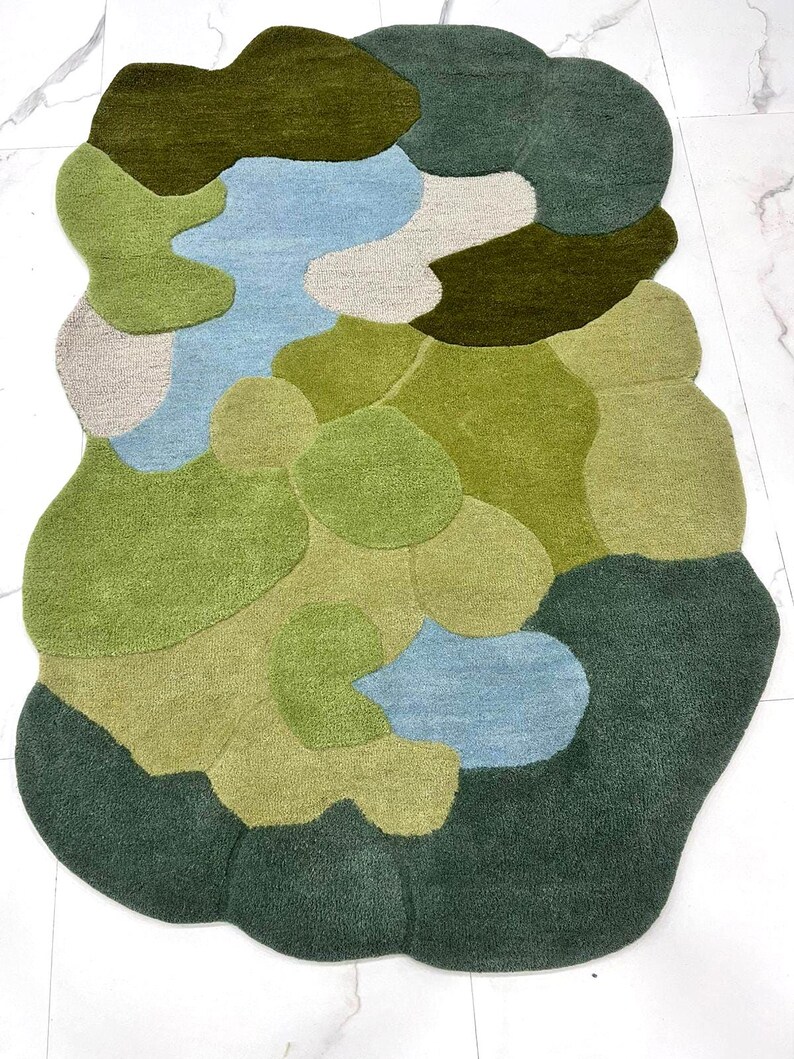 Overhead view of a hand-tufted wool rug with an irregular organic shape in shades of green and blue on a white marble floor.